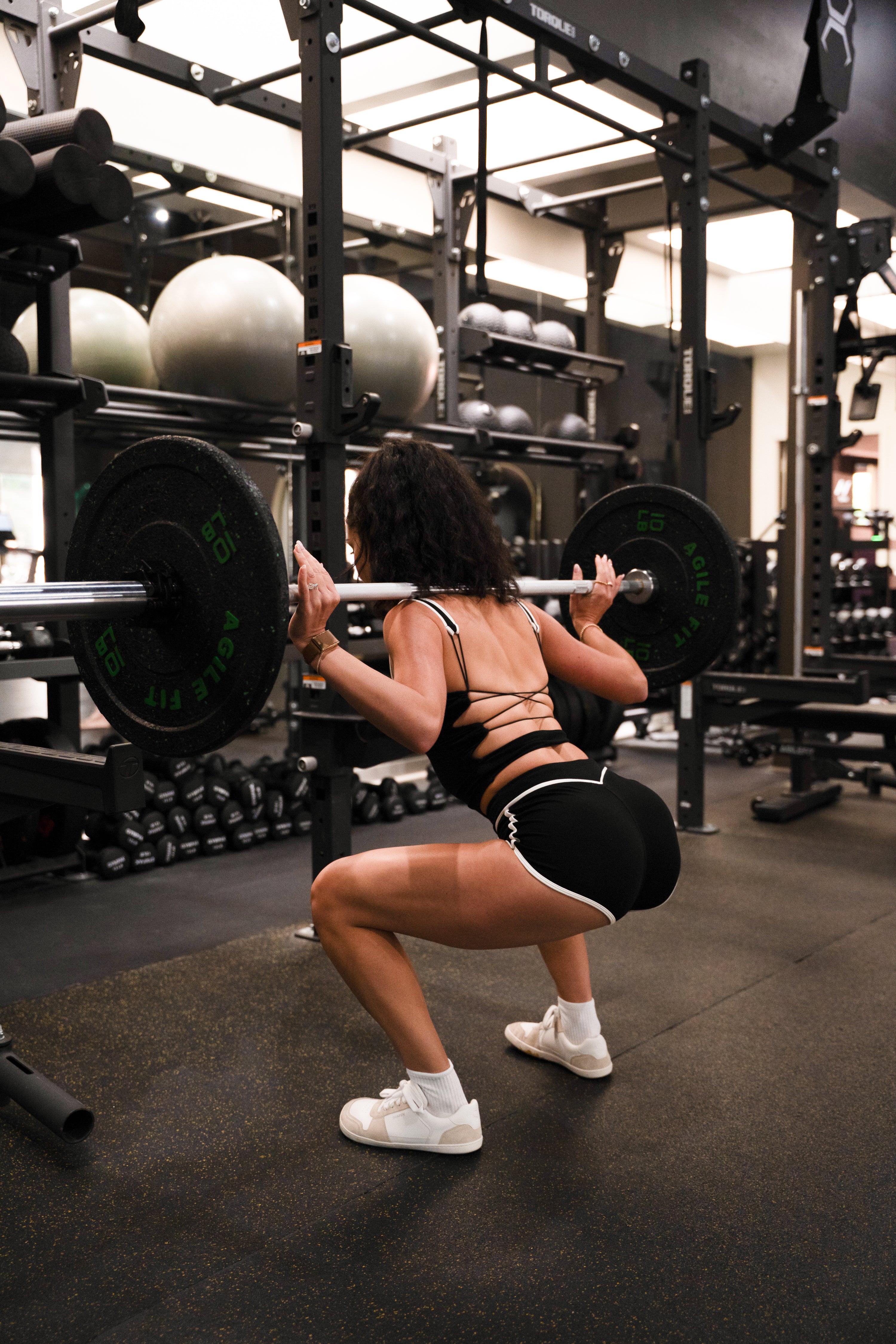 Woman performing squats with a barbell in a gym setting with non-toxic activewear